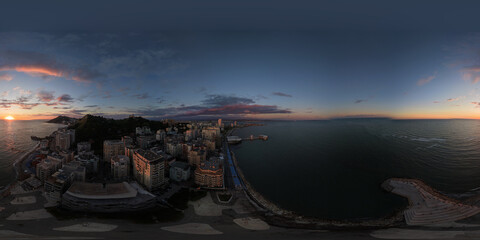 Blue-hour aerial panorama of a curving bay, waterfront high-rises and deepening evening sky over the sea. © Ndue