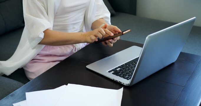Woman multitasks efficiently. Individual switches between digital tools to handle various responsibilities. Woman seamlessly navigates between her phone and computer to review and plan tasks