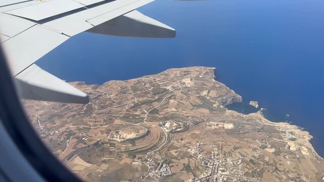 Airplane window view flying over Malta with aircraft fuselage and wing visible