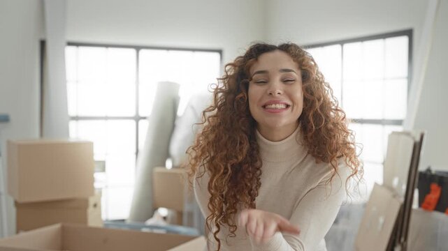 Woman with moving boxes and open carton blowing a kiss while reaching hand forward in studio; joyful new home.