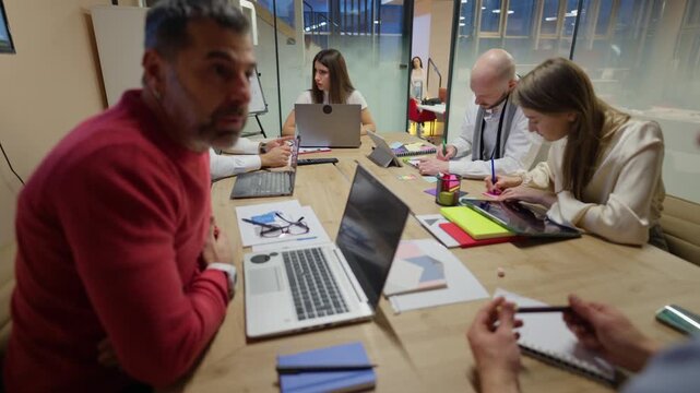 Employees actively participate in a collaborative business meeting at the office. Coworkers engage in an important discussion, sharing ideas and working together.