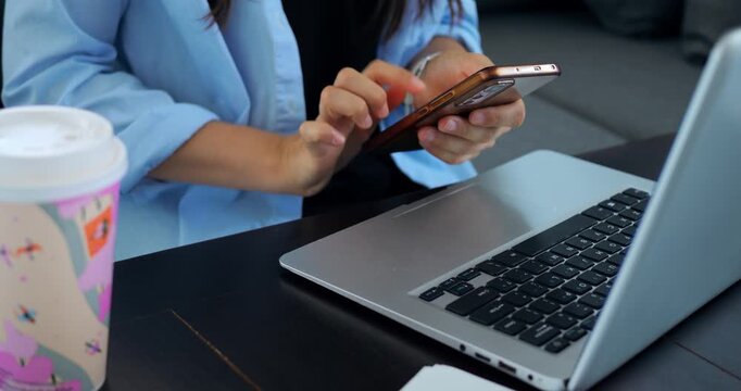 Woman shopping online. Woman examines retail applications on her smartphone near laptop. Female individual analyzes various online store selections using her phone and computer simultaneously