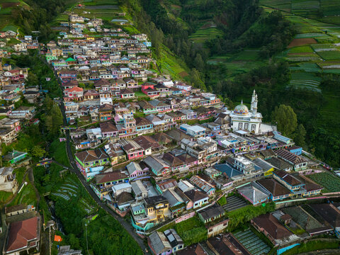 Aerial view of the colorful houses of Butuh village and the Baituttaqwa Mosque nestled on the steep terraced slopes of Mount Sumbing in Kaliangkrik, Central Java, Indonesia.