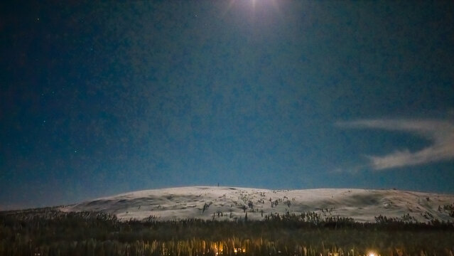 Aerial view of Luosto fell covered in snow under a starry night sky with the moon shining above the horizon in Sodankyla, Lapland, Finland.