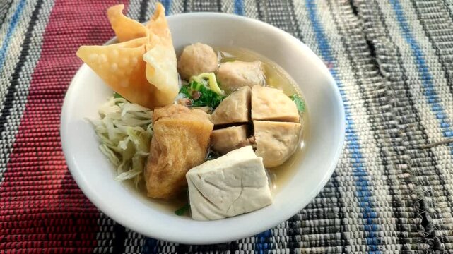 Close up video of delicious bakso meatball soup in white bowl on simple mat, authentic Indonesian street food with warm taste