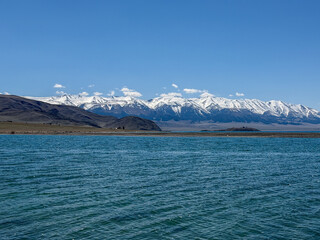 Obraz premium Beautiful scenic view of Sayram Lake with turquoise water and snow-capped Tianshan mountains in Xinjiang, China.