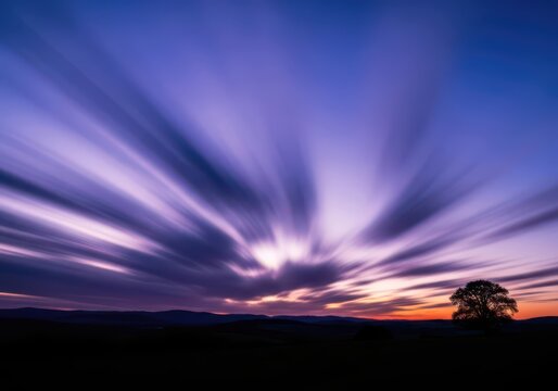 Sun rays breaking through dramatic twilight sky with silhouette tree