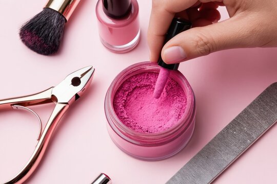 Woman dips nail polish brush into pink powder. Manicure tools like clippers and file are nearby. Beauty salon supplies create nail art. Pro care for hands.
