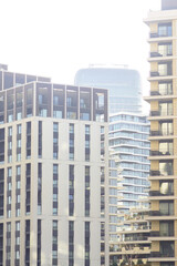Fototapeta premium Modern towers of different heights emerge through morning haze above newly built district. Shows vertical densification trends, speculative construction expansion, layered contemporary city growth.