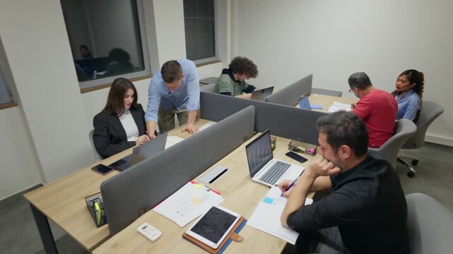 People are busy working and collaborating in a contemporary open-plan office. Coworkers engage in their daily tasks and discussions at their desks.