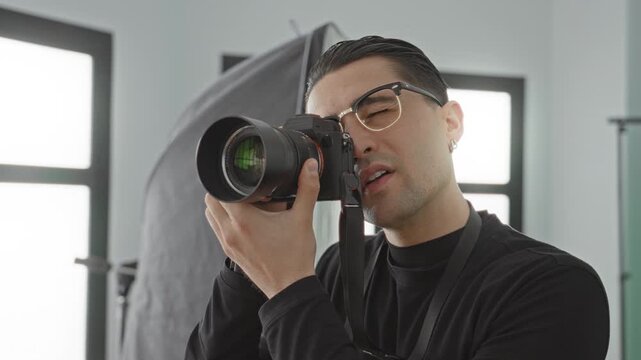 Man holding dslr camera to eye, hand on lens and looking through viewfinder in studio; concentration creativity.