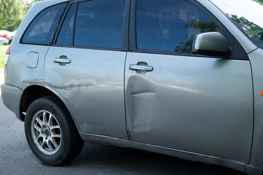 Close-up of a dented and scratched silver car door after a traffic accident, auto body damage concept.