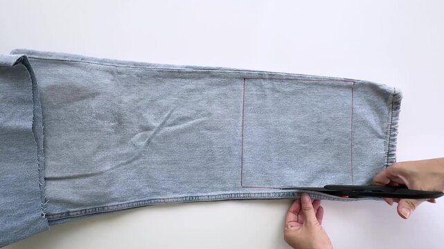Woman Cutting Light Blue Denim Fabric from Old Jeans for DIY Sewing and Upcycling Project
