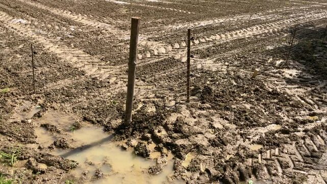 Agricultural field in the rural countryside and metal fence barrier, tilled and prepared for planting crops, muddy ground or soil with furrows and tractor tire tracks in Germany, Europe