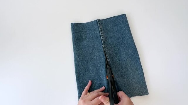 Woman Cutting Light Blue Denim Fabric from Old Jeans for DIY Sewing and Upcycling Project

