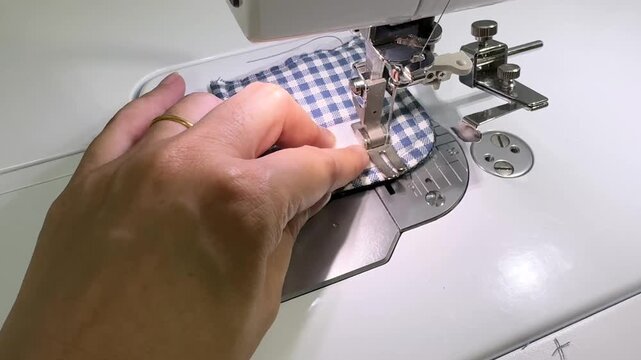 A woman is sitting and sewing with a sewing machine.