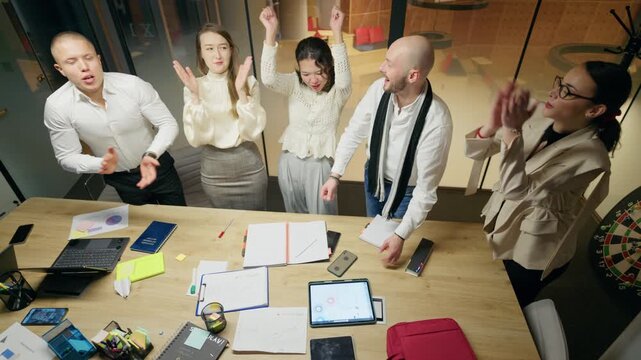 A business team celebrates success during an office meeting, giving high fives and showing excitement. Happy colleagues collaborate and rejoice after achieving a positive outcome in their project.