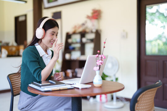 Asian young women remote working from cafe using laptop computer headphones video call conference meeting online at coffee shop with notebook smiling happy