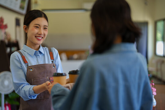 Asian female barista serving customer at cafe counter smiling welcoming guest small business owner working hospitality service retail shop interior cafe worker
