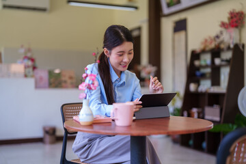 young Asian women smile using tablet computer browsing online shopping ecommerce reading digital content working at cafe coffee shop remote work casual © Pichsakul
