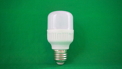 A single LED light bulb stands upright against a bright green background. © anungcamui