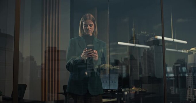 Businesswoman Using Smartphone App Behind Glass Office Window Overlooking Futuristic Cityscape With Autonomous Delivery Drones Flying Past Skyscrapers, Symbolizing Digitalization and Smart Technology.