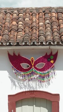 M&aacute;scara festiva rosa decorando fachada branca de casa colonial com telhado de barro em Tiradentes, MG. Simplicidade e tradi&ccedil;&atilde;o na folia mineira.