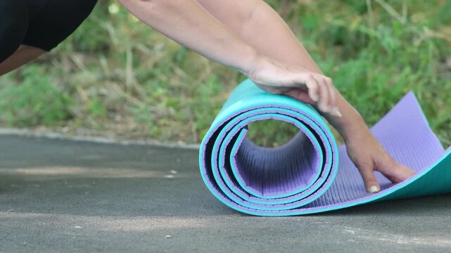 Female hands unrolling blue yoga mat on ground during outdoor workout. Concept of starting fitness routine and physical activity in nature.