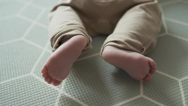 Little infant legs and bare feet moving on a floor mat, babyhood concept.