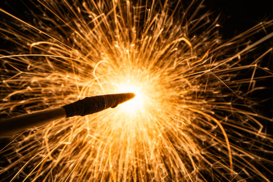 Macro shot of bright golden sparks flying from a burning sparkler or pyrotechnics on a black background
