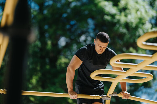 A fit man performs calisthenics on yellow parallel bars at an outdoor park. He focuses on strength training during a sunny bodyweight workout.