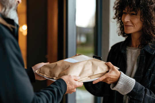 This image captures a warm moment of delivery as a smiling woman receives a package from a courier, highlighting human connection and service-oriented interactions.