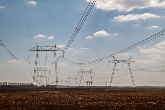 High voltage electrical transmission towers in agricultural landscape under blue sky. Power lines infrastructure for energy distribution and electricity transmission