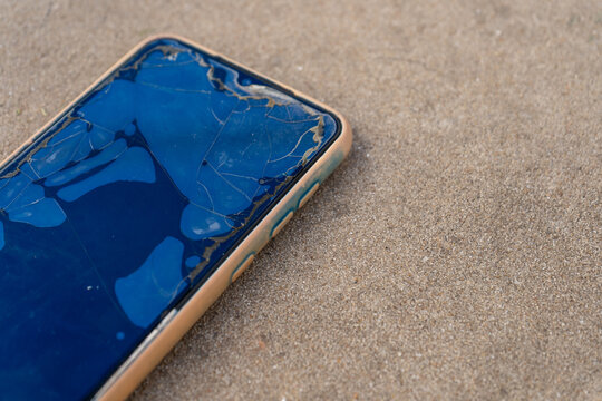 Broken smartphone screen with cracked glass protector on concrete surface, damaged mobile phone device