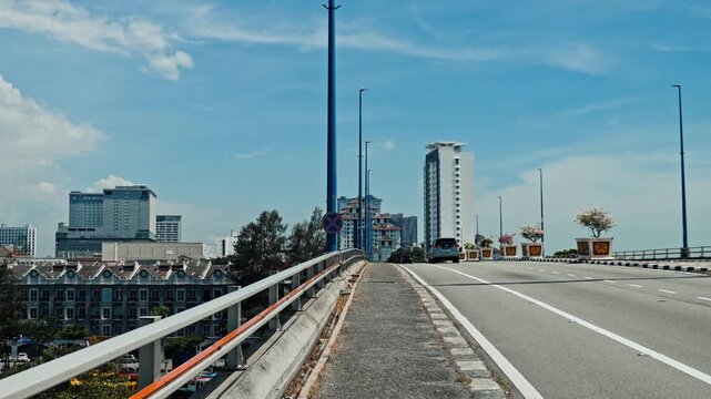 Malacca, Malaysia, 16 Nov 2025. Bridge road leading towards modern city skyline with high-rise buildings under blue sky, urban infrastructure and development, editorial documentary.