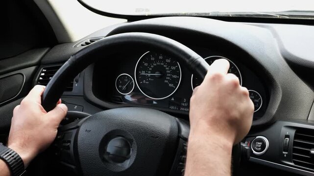 Male arms holds steering wheel while driving a motor car at city. Young man riding on electric automobile at urban road. Driver moving on his electrical auto on route. Slow motion
