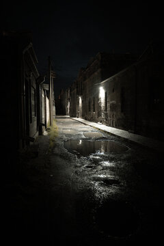 Night scene of empty urban alley with puddles reflecting lights