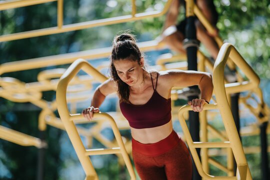 A fit woman performs a dip exercise on yellow outdoor calisthenics bars. She focuses on strength training and a bodyweight workout in a park fitness area.