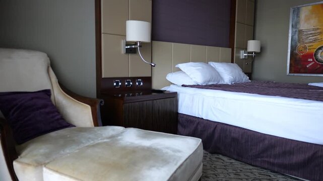View of modern hotel room interior with neatly arranged bed, soft day lighting and comfortable furniture. Cozy accommodation space designed for relaxation, travel and hospitality service