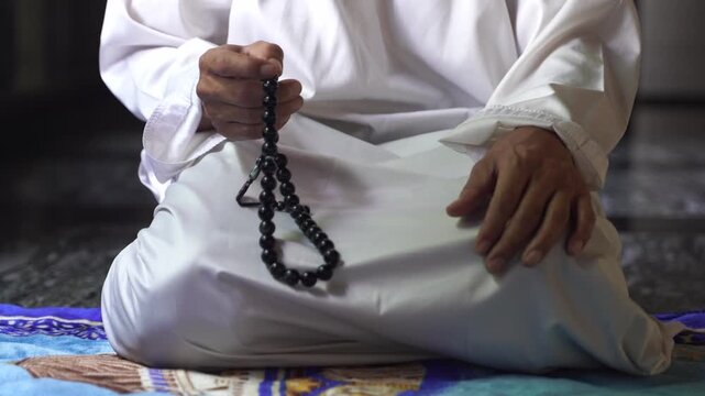 Muslim man holding and counting Islamic prayer beads (Misbaha) close up, spiritual devotion and faith inside peaceful mosque.
