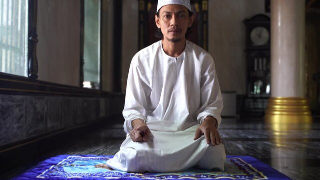 Muslim young man sitting in Tashahhud position during Salah prayer inside mosque.