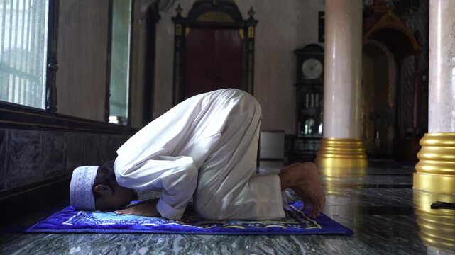 Devout Muslim man prostrating (Sujud) in prayer on a rug inside mosque.