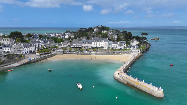 Aerial view of the coastal town of Locquirec featuring a sandy beach, stone pier, and traditional houses overlooking turquoise waters in Locquirec, Brittany, France.