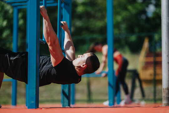 A man performs an inverted row on blue parallel bars for a bodyweight strength workout. He trains at an outdoor fitness park while another person exercises in the background.