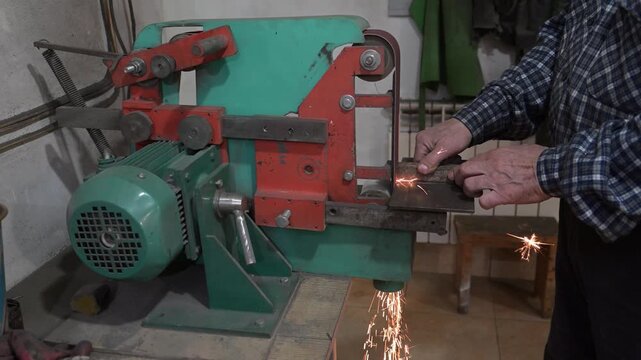 An electric machine for grinding metal in the production room of the workshop. The process of working on a metal-sanded grinding machine with working hands