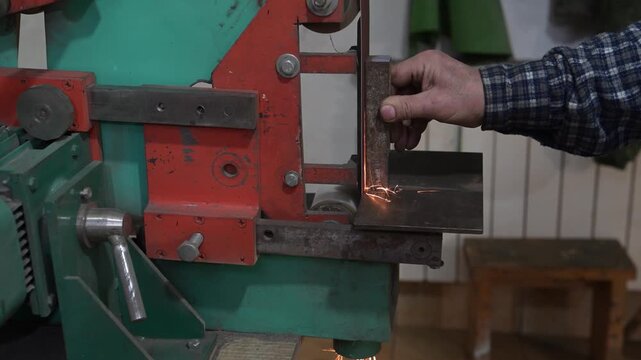 An electric machine for grinding metal in the production room of the workshop. The process of working on a metal-sanded grinding machine with working hands
