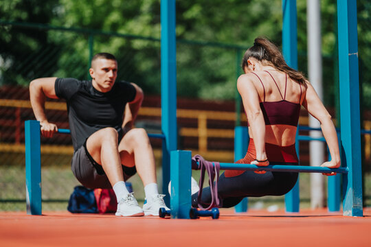 A man and woman perform dips and bodyweight exercises on parallel bars in an outdoor park. The couple trains together doing calisthenics and strength workout on a sports court.