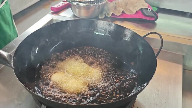 Chef deep frying hard boiled eggs in a hot wok.