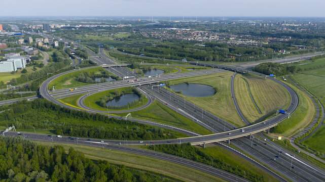 Aerial view of the Knooppunt Oudenrijn highway interchange with complex road networks, green meadows, and small ponds in Utrecht, Utrecht, Netherlands.