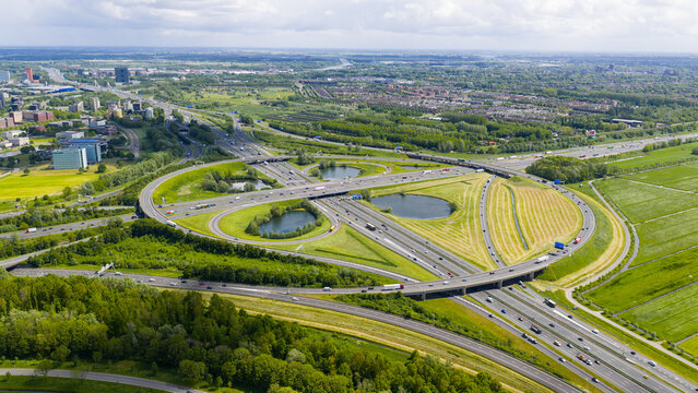 Aerial view of the Knooppunt Oudenrijn highway interchange with green fields and circular loops under a bright sky in Utrecht, Utrecht, Netherlands.